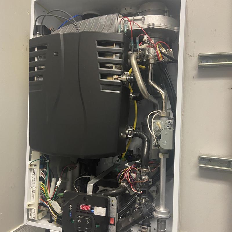 Tankless water heater with exposed wiring and pipes