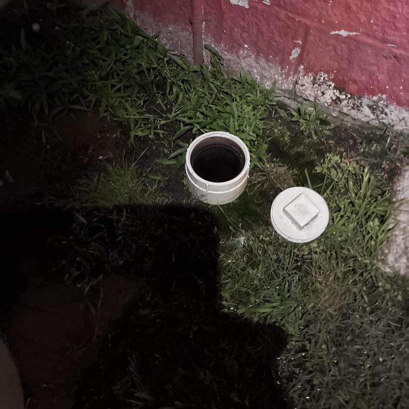 Sewer cleanout pipe and cap by red wall at night