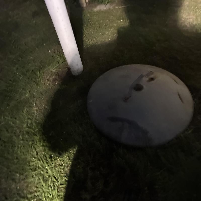 Septic tank lid beside white vent pipe at night