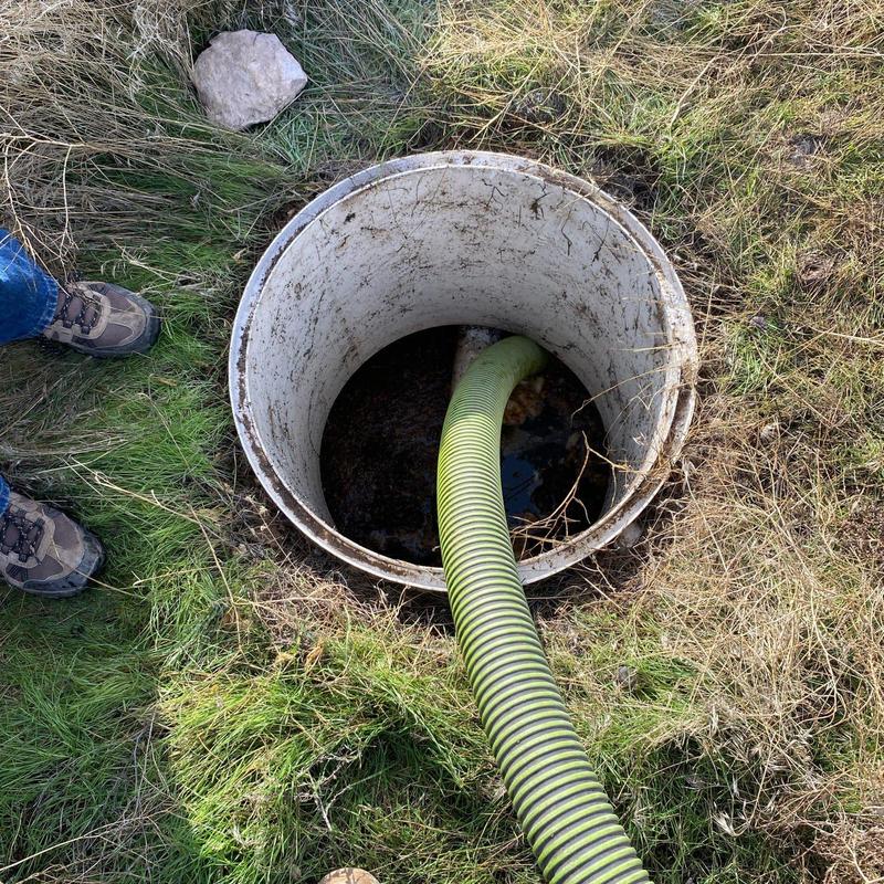 Septic tank with green pump hose in grassy area