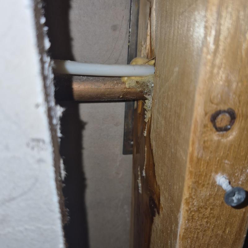 Copper water pipe with plastic tubing through drywall hole Copper water pipe with plastic tubing through drywall hole