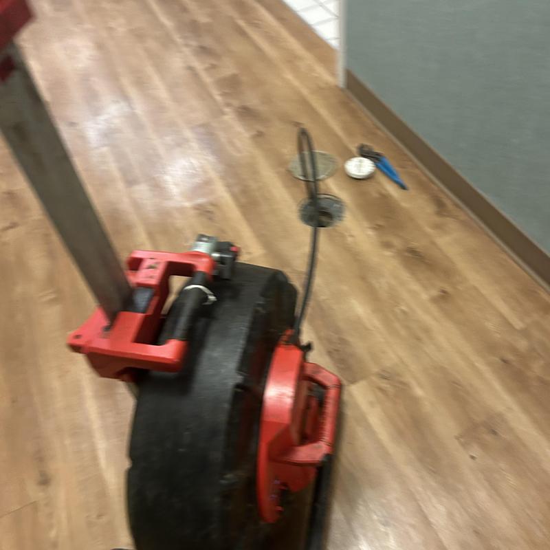 Main line drain auger machine on wood floor near pipe access Main line drain auger machine on wood floor near pipe access