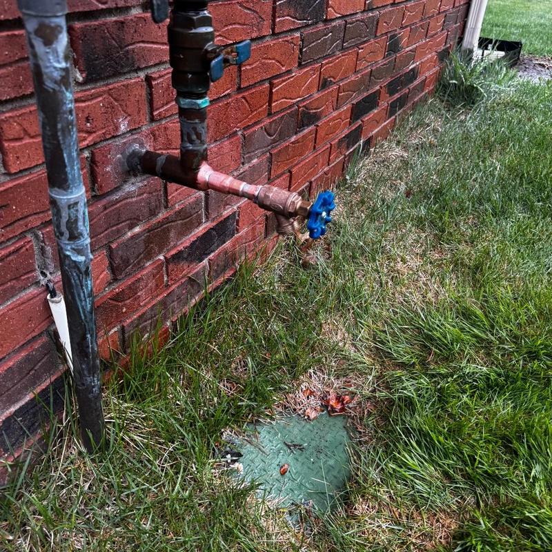 Outdoor hose bib valve with blue handle on brick wall