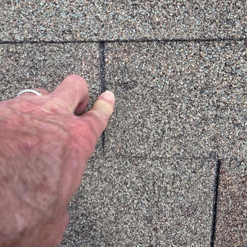 Asphalt roof shingle hail damage close-up with hand