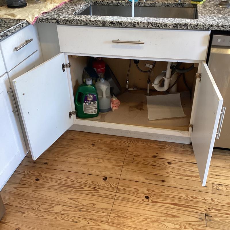 Kitchen sink drain pipes under cabinet with cleaning supplies