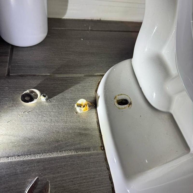Toilet base with broken mounting hardware on tile floor