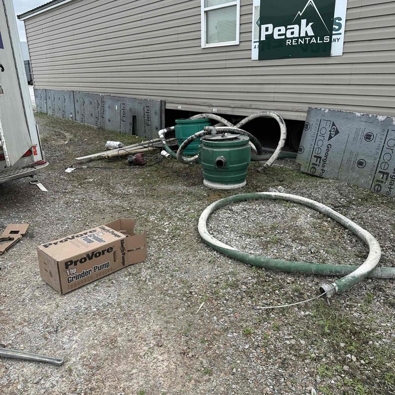 Grinder pump and pipes beside mobile home exterior