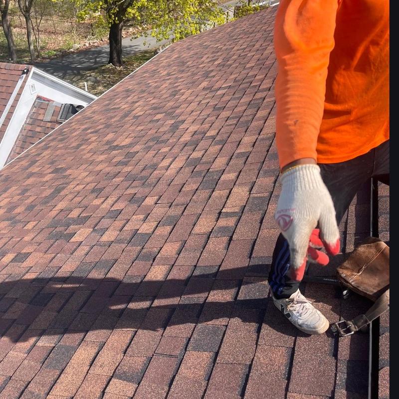 Asphalt shingle roof installation with worker in orange shirt