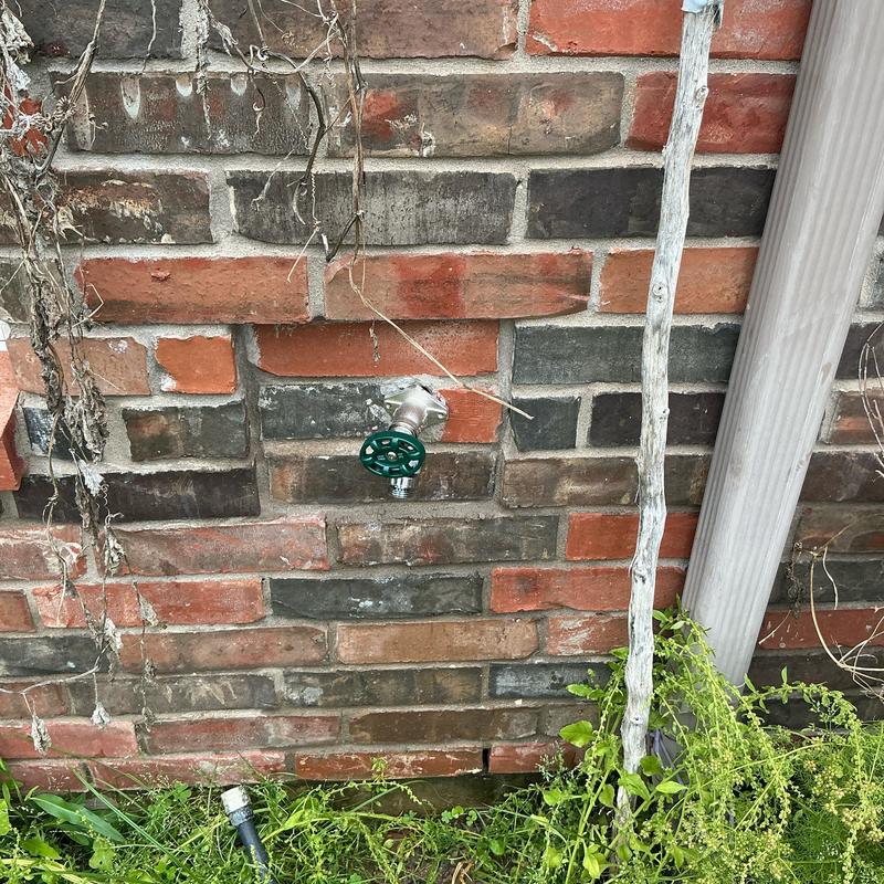 4-inch hose bib with green handle on brick wall