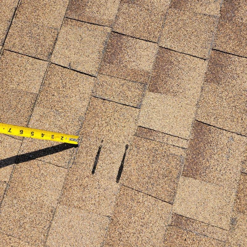 Asphalt shingle roof with visible damage and measuring tape