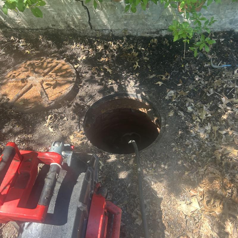 Sewer jetting hose inside open manhole in dirt ground