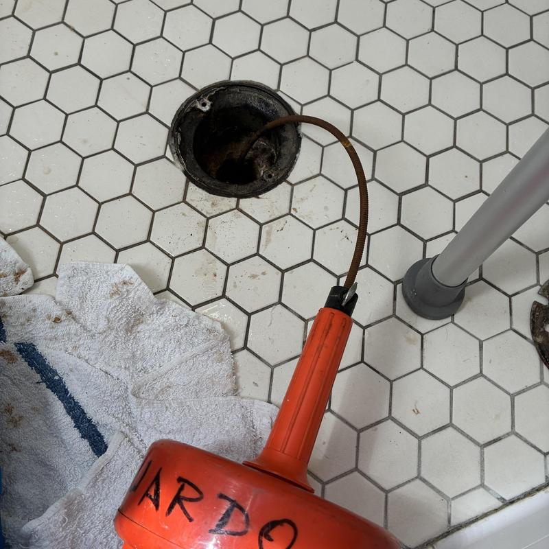 Shower drain cabling tool clearing clog on tile floor Shower drain cabling tool clearing clog on tile floor