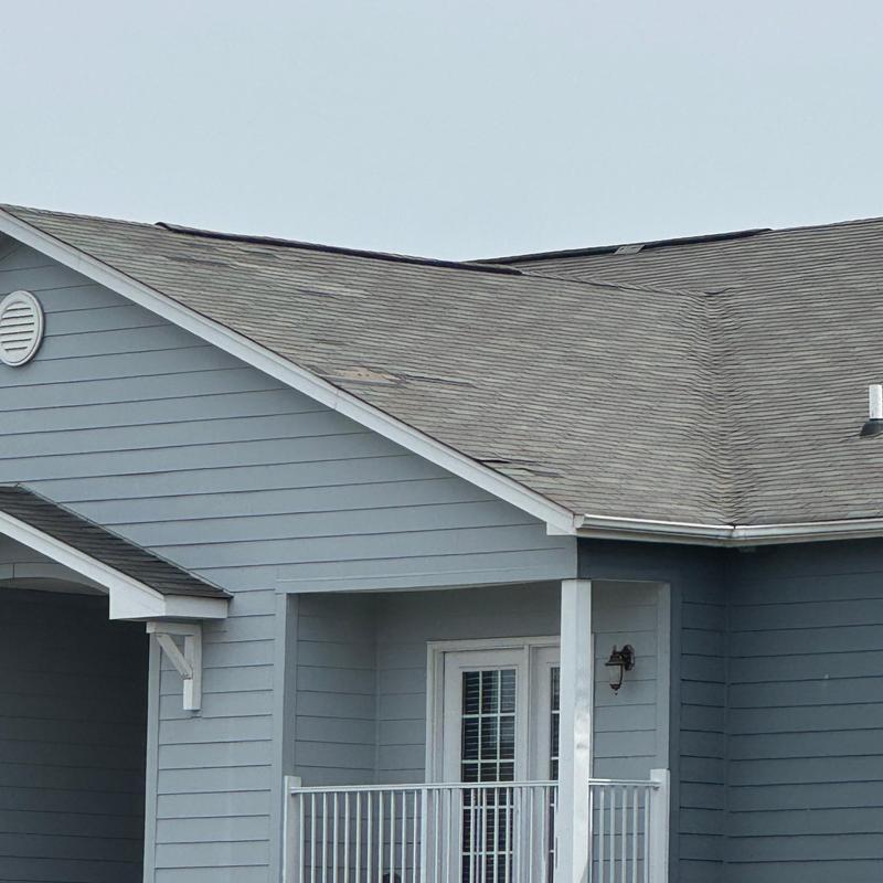 Asphalt shingle roof with visible damage on apartment building
