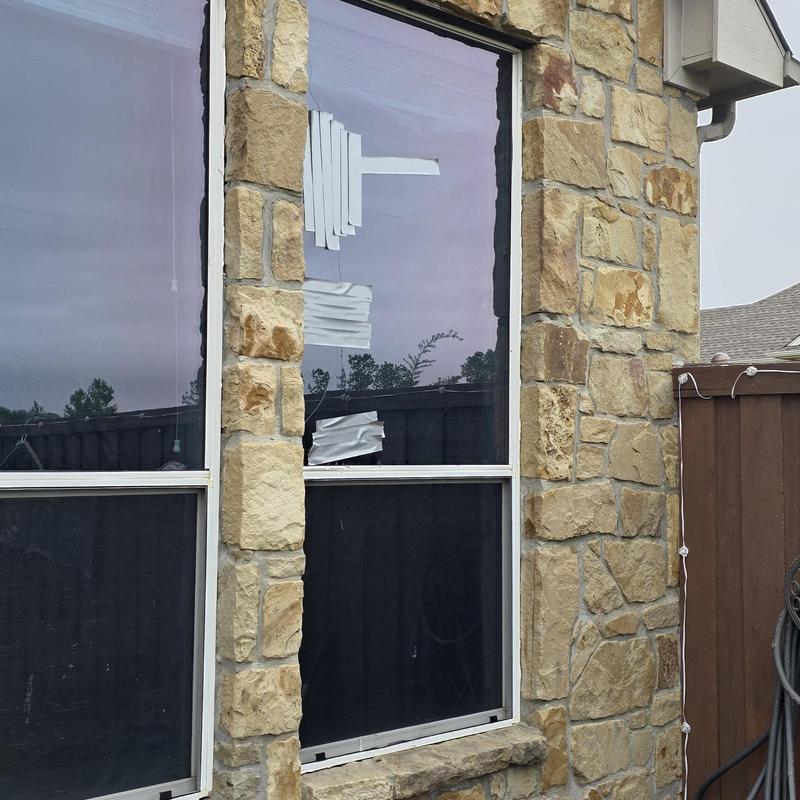 Window glass with tape covering hail damage in stone wall
