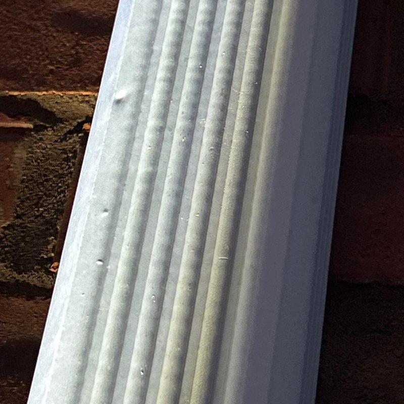 Metal gutter with hail damage dents on house exterior