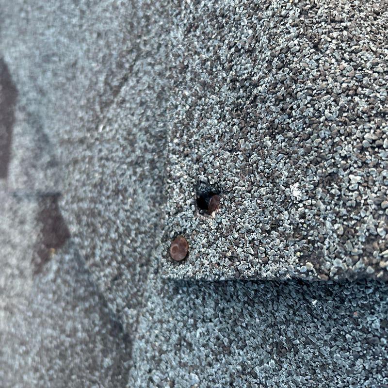 Asphalt roofing shingles with hail-damaged nail head exposed
