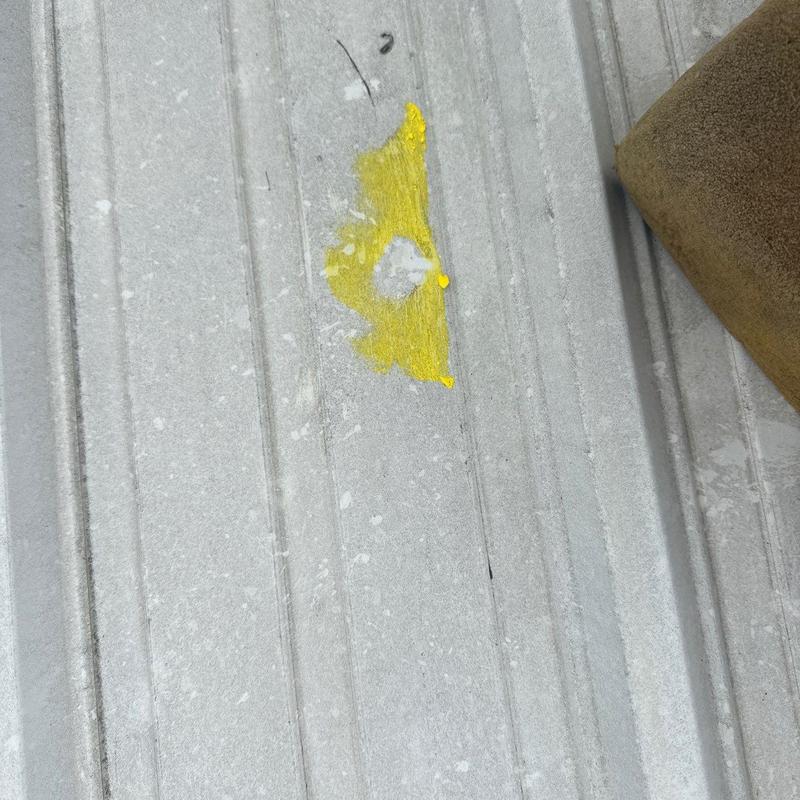 Metal roof panel with hail damage marked in yellow