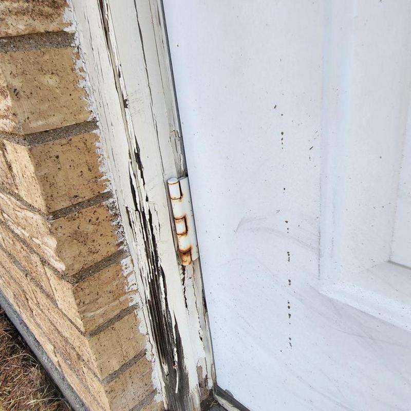Exterior door trim with peeling paint and rusted hinge