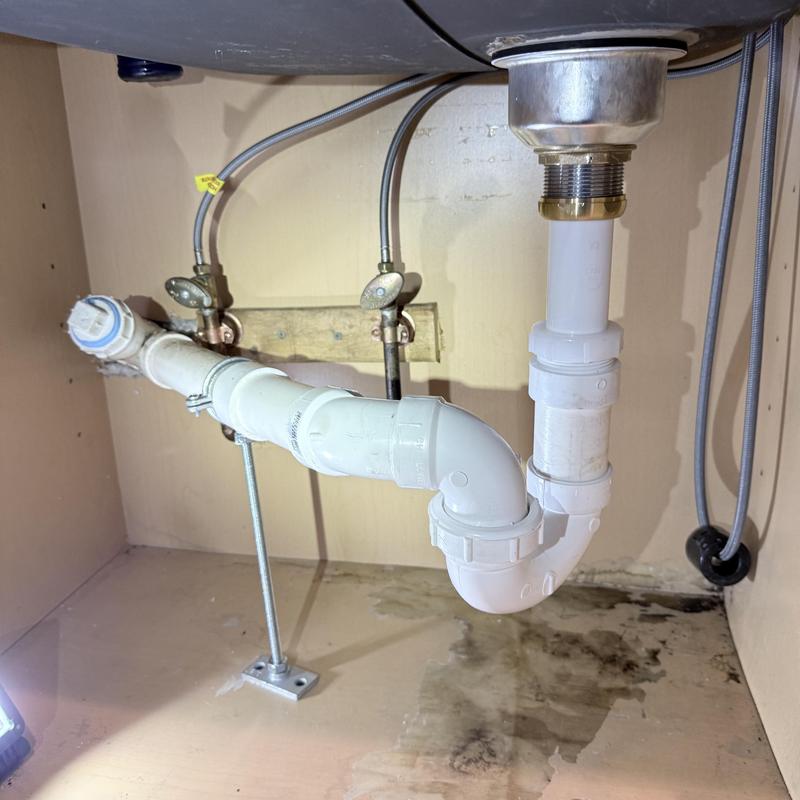 Kitchen sink drainage pipes under cabinet with leak stain