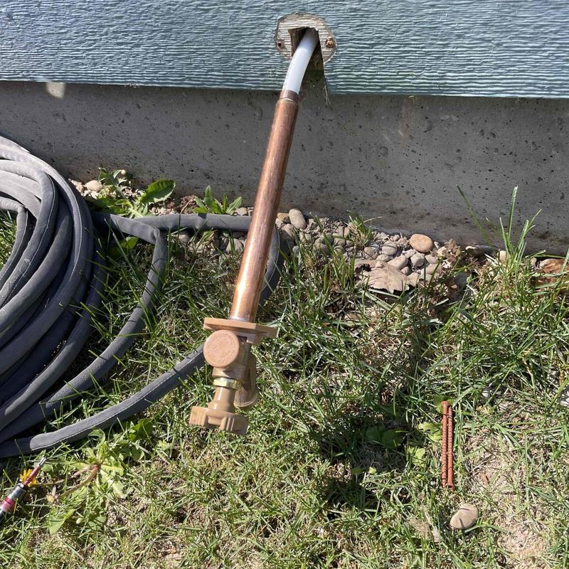 Outdoor hose bib with copper pipe and garden hose nearby