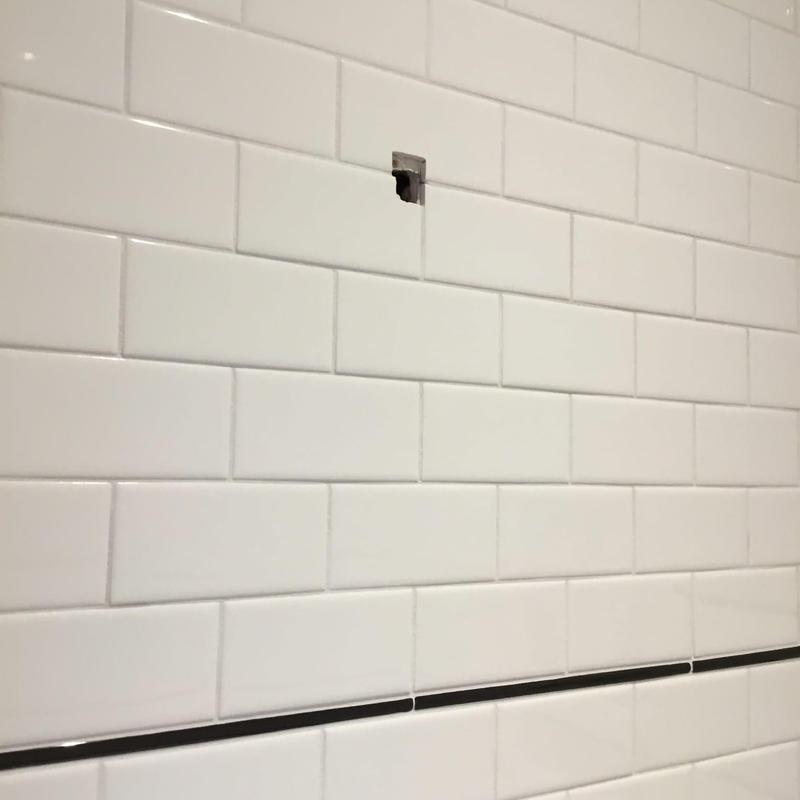 Shower valve opening in white tiled bathroom wall