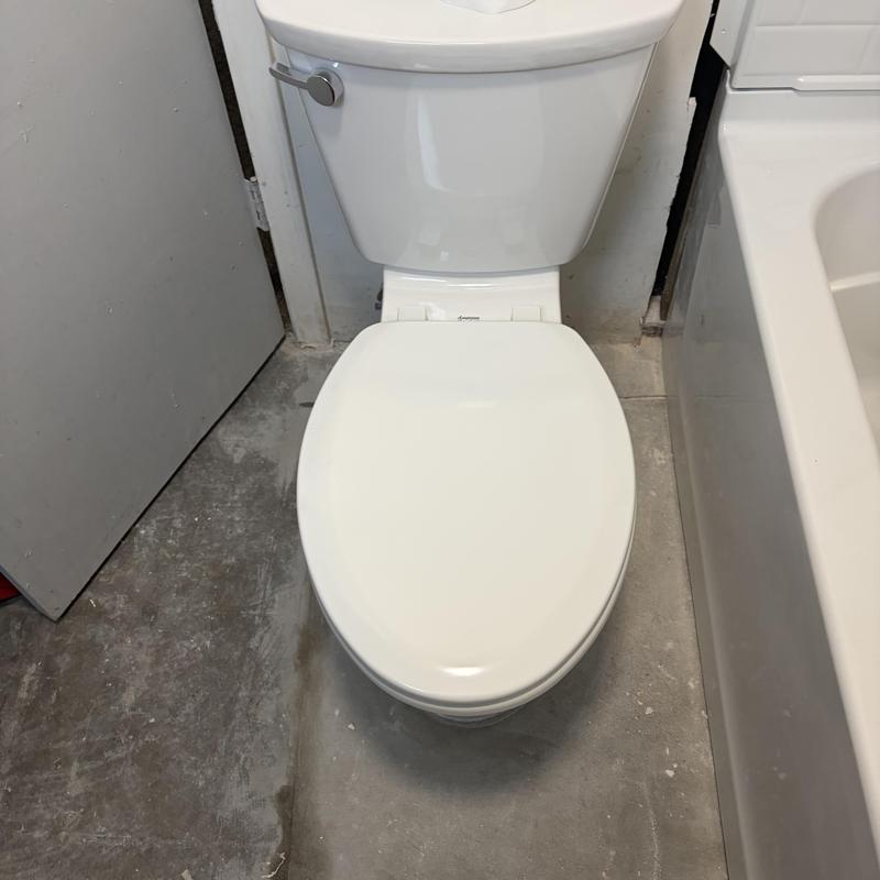 Toilet installation on concrete floor near bathtub