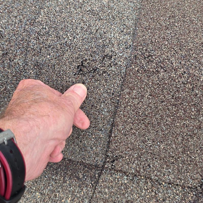 Asphalt shingle roof hail damage close-up with hand