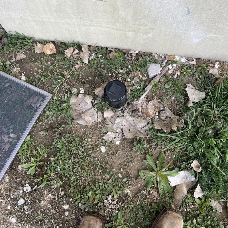 Sewer cleanout in backyard surrounded by soil and leaves