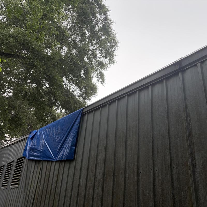 Metal building roof with blue tarp covering damage