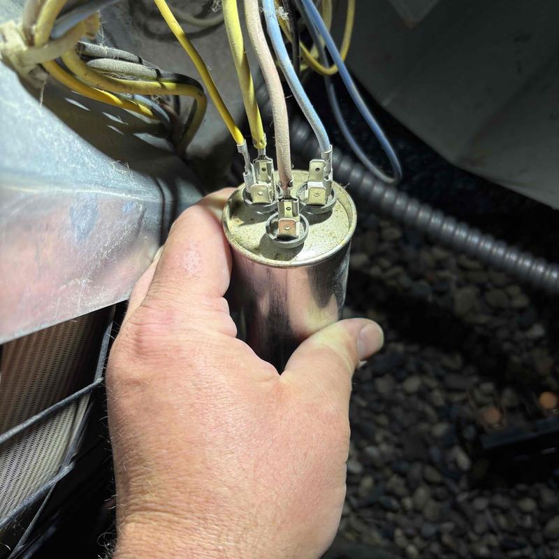 Dual run capacitor held by hand near HVAC unit wiring