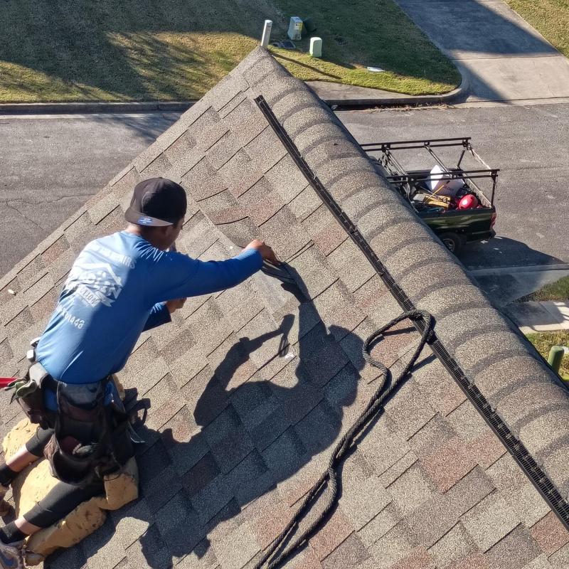 Asphalt shingle roof with worker repairing wind damage