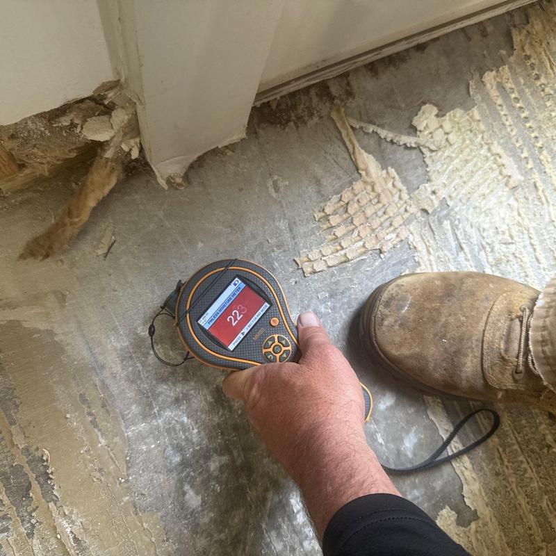 Moisture meter detecting floor water damage near wall baseboards