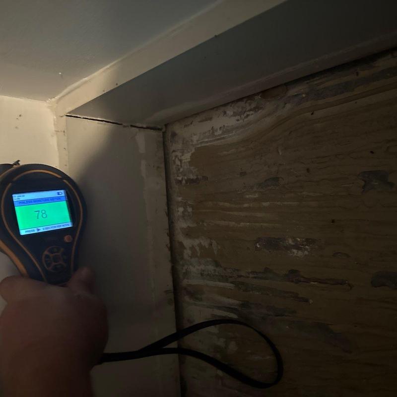 Moisture meter detecting wall moisture near basement corner