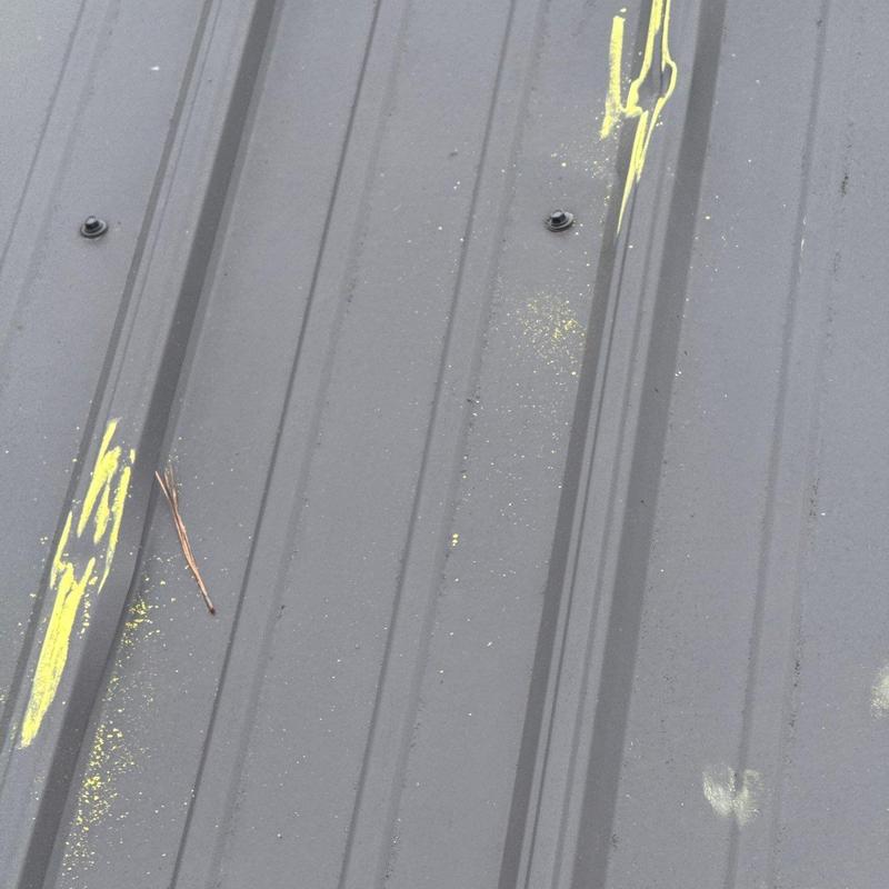 Metal roof panel with hail damage marked in yellow
