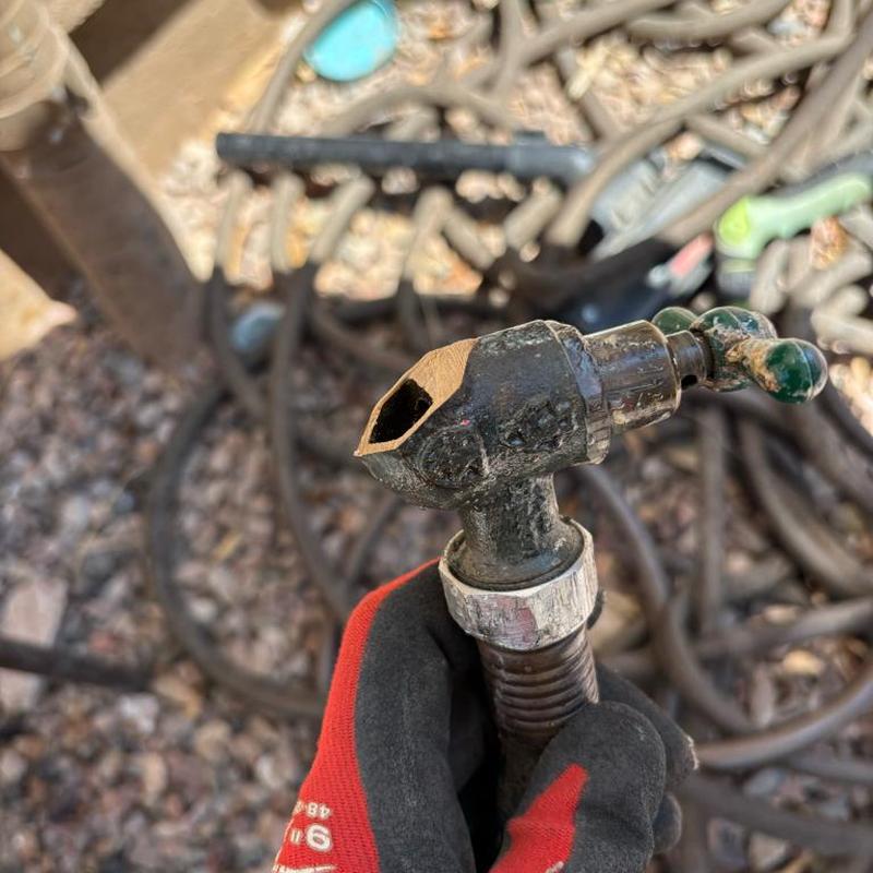 Frozen hose bib with cut-off hose held by gloved hand
