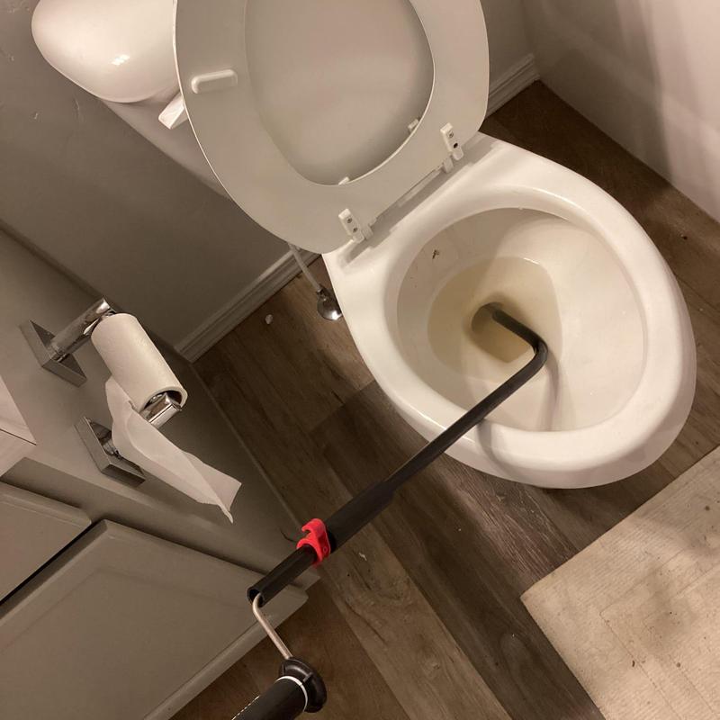 Toilet with auger stuck inside bowl during plumbing work