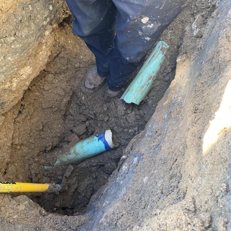 Broken underground sewer pipe exposed in dirt trench