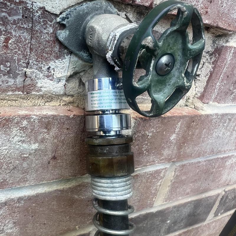 Outdoor hose bib with metal valve handle on brick wall