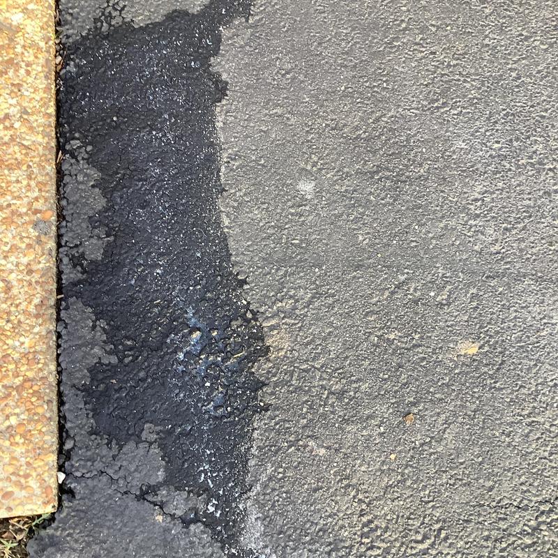 Asphalt driveway patch showing fresh sealant edge