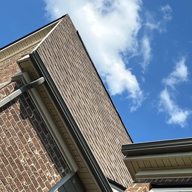 Asphalt shingle roof with gutter and downspout detail under blue sky