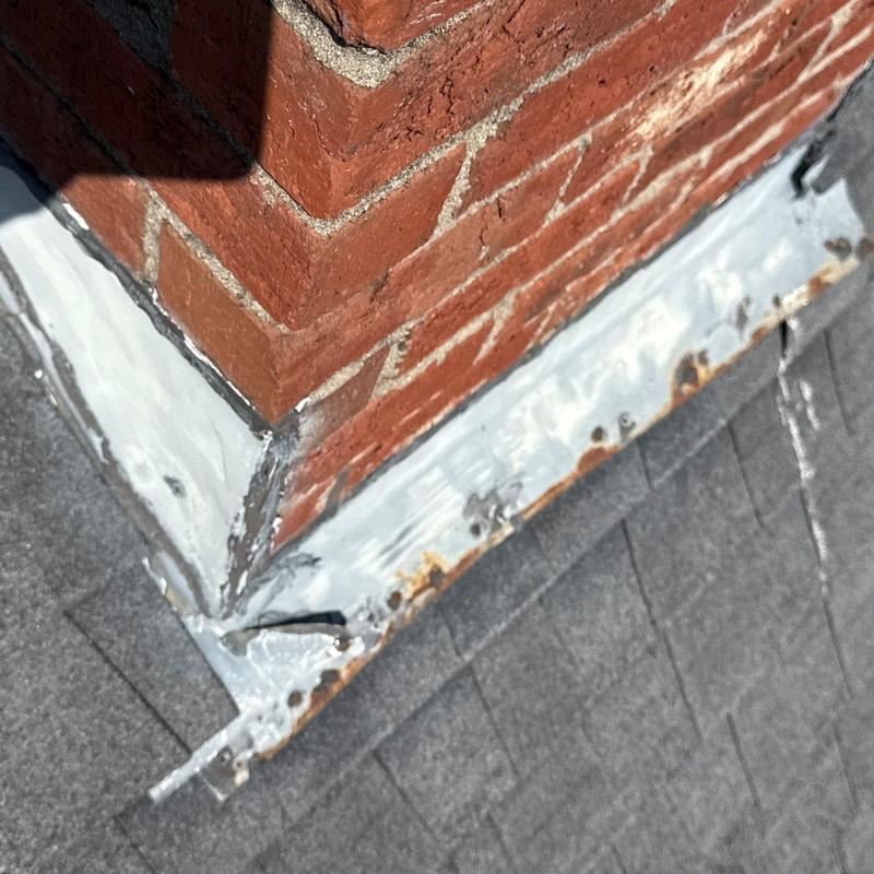 Chimney flashing with rust and sealant on shingled roof