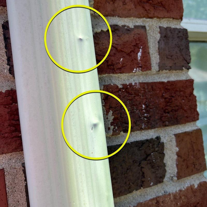Metal downspout with hail damage dents on brick wall