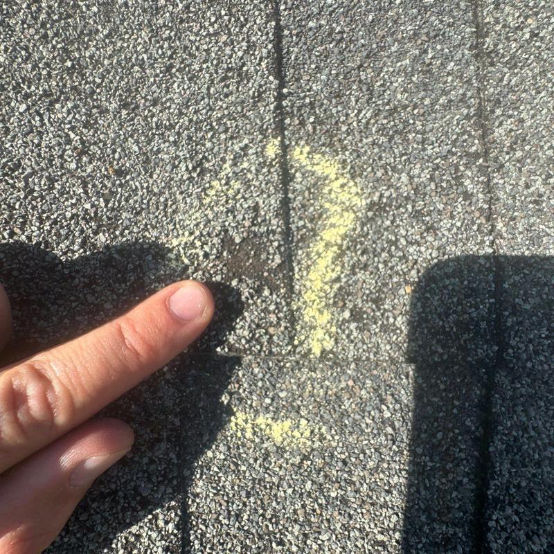 Asphalt shingle with hail damage marked by yellow arrow
