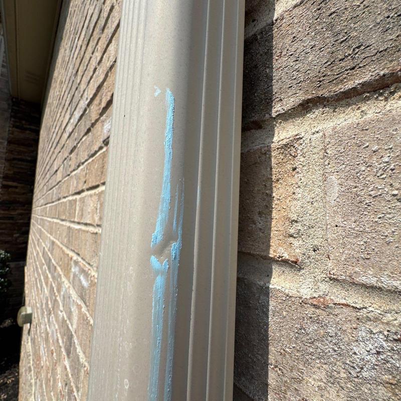 Downspout with blue paint smear near brick wall