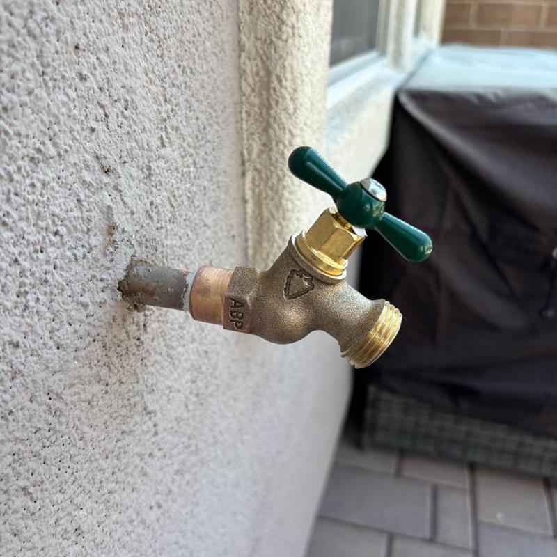 Hose bib replacement with green handle on exterior wall