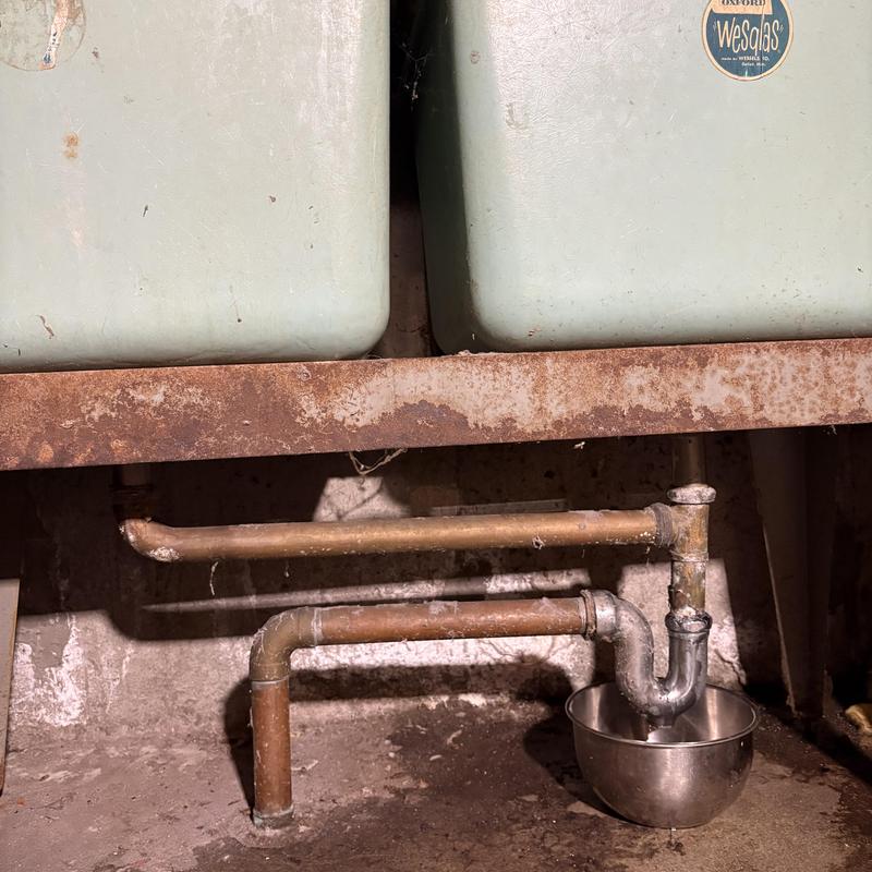 Copper drain pipes under laundry sinks with rusted support