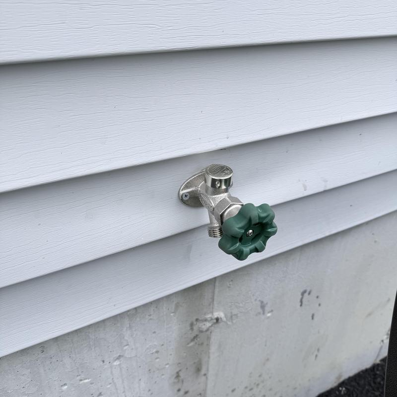 Silcock faucet with green handle on house siding