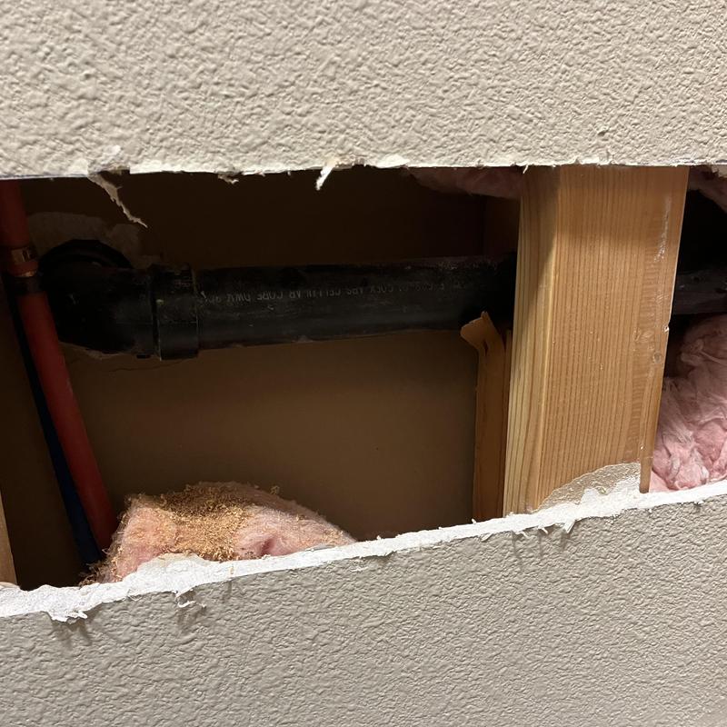 Black PVC drain pipe inside cut drywall for leak search