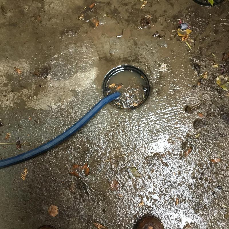 Area drain with hose vacuuming mud buildup outdoors