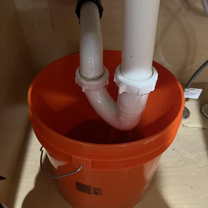 Kitchen sink drain pipes over orange bucket under cabinet